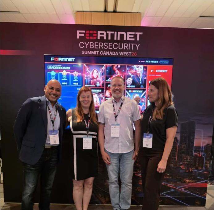 Four attendees posing in front of the live social wall and leaderboard.