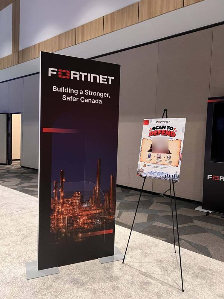 A Scan to Defend poster on an easel beside a branded banner on the summit floor.